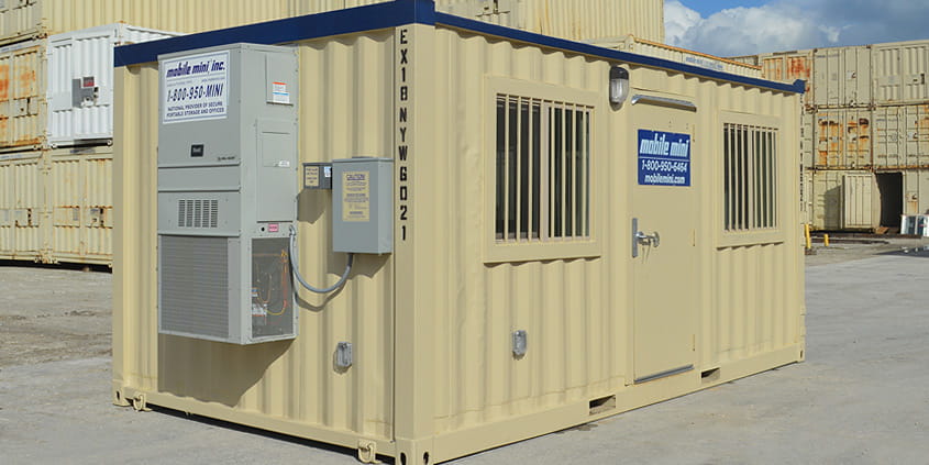 Equipped mobile office trailer shown among stacks of storage containers